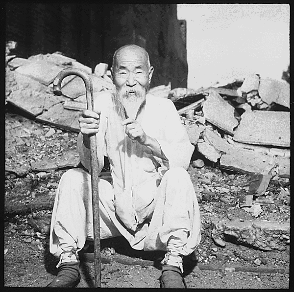 An old Korean man takes a rest on the street in front of destroyed buildings, in Seoul., 08/20/1951